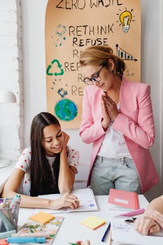 A teacher in a pink blazer smiles while guiding a student at a desk in an eco-friendly classroom.