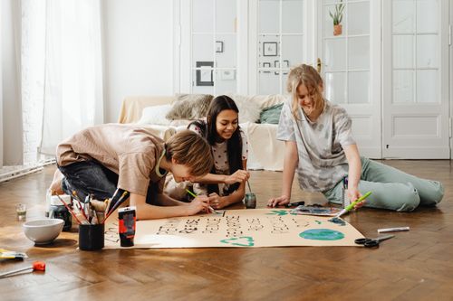 Free Group of teens engaging in a creative art project indoors, emphasizing teamwork and creativity. Stock Photo