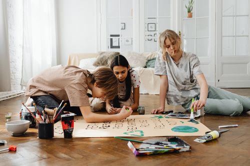 Free Three teenagers collaborate on an art project, painting on a poster indoors. Stock Photo