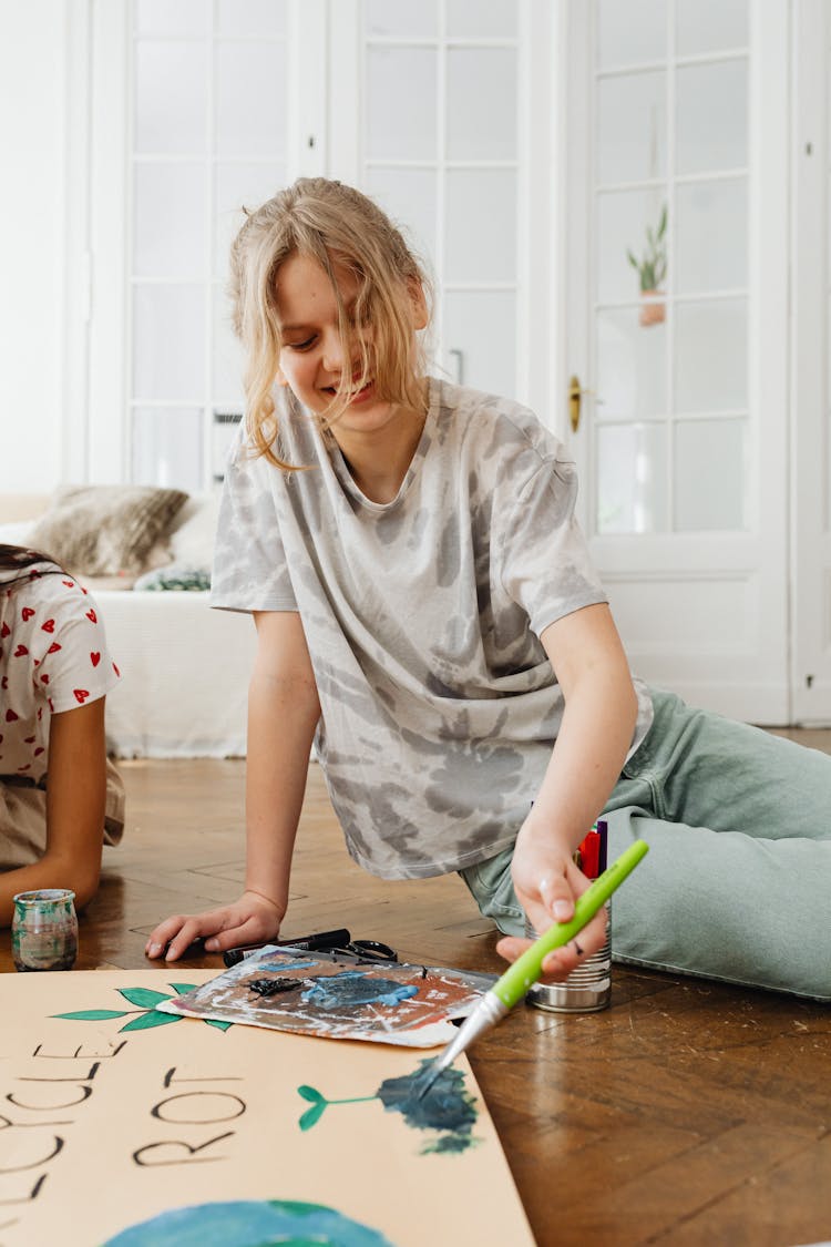 Smiling Blonde Girl Painting On Floor