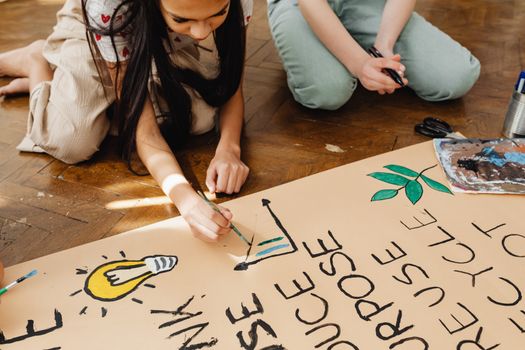 Two teenagers painting a poster about recycling and environmental awareness for a school project.