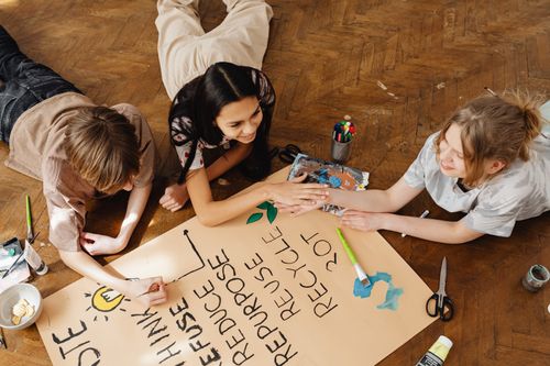 Free Three teenagers collaborate on an eco-friendly poster, promoting sustainability with creativity indoors. Stock Photo
