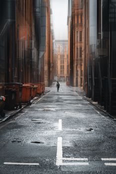 A solitary figure walks down a wet alleyway flanked by city buildings in Manchester, UK.