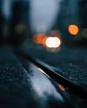 Close-up of a wet road with blurred city lights, creating a moody ambiance.