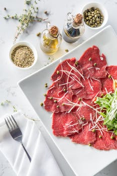 白色盘子上摆放着美味的牛肉片，配以刺山柑、橄榄油和新鲜配料