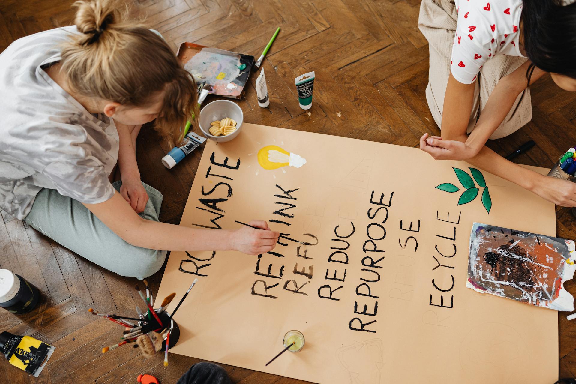 Top view of two young adults crafting an eco-friendly sign emphasizing recycling and repurposing.