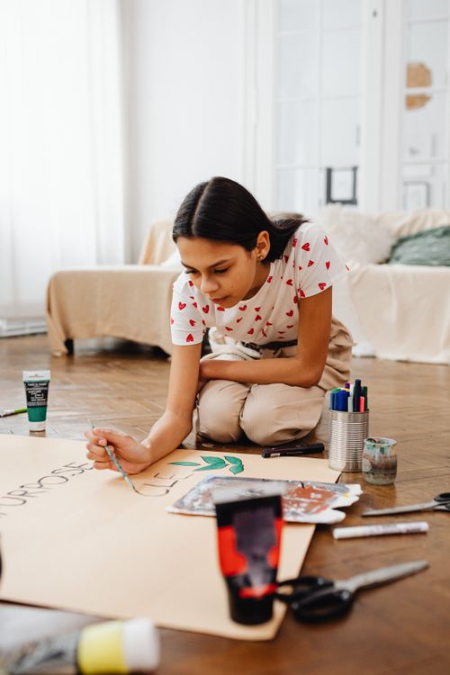 Free Creative young girl focused on painting artwork indoors, surrounded by art supplies. Stock Photo