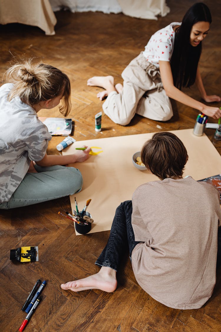 Teen Students Painting The Banner While Sitting On The Flor