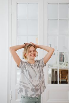 Smiling woman posing with hands on hair in bright indoor space.