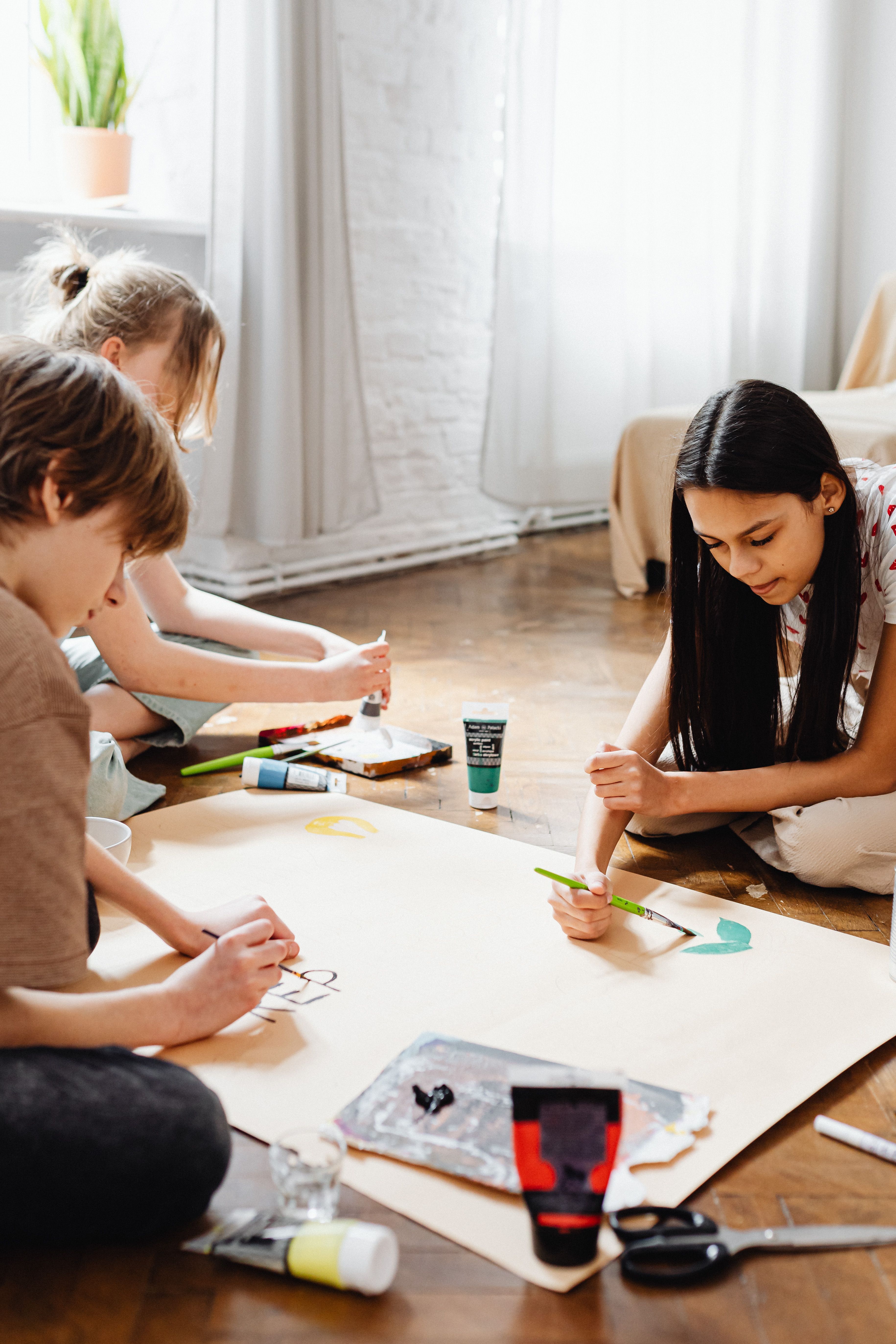 Three kids working together on a painting project indoors, showcasing creativity and teamwork.