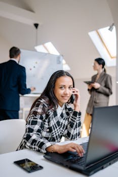 Confident businesswoman smiling while working on laptop in modern office with colleagues.
