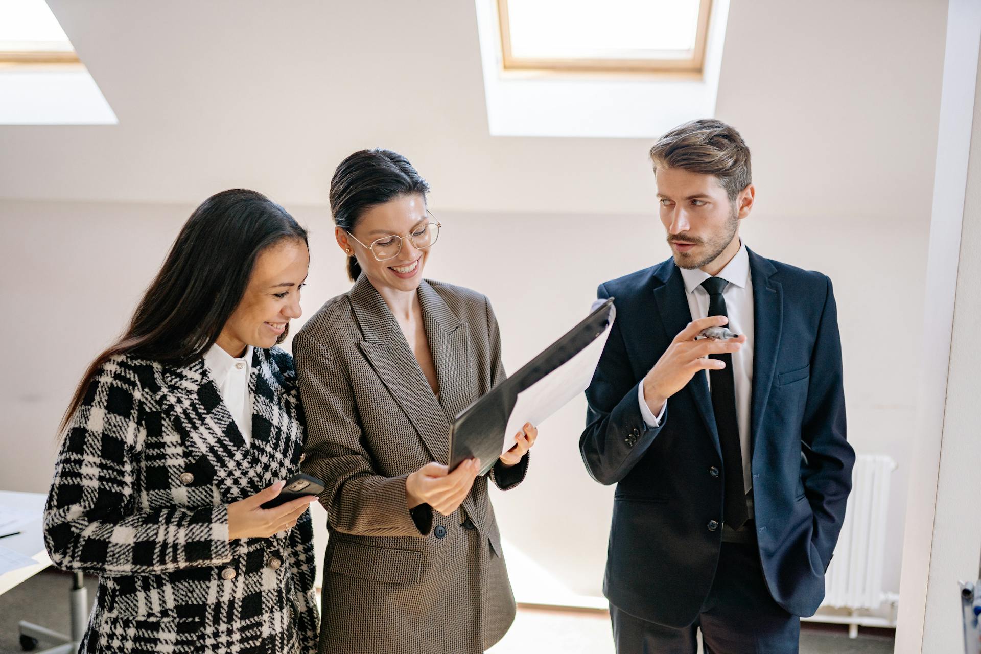 A diverse team of three colleagues discussing documents in a bright office.