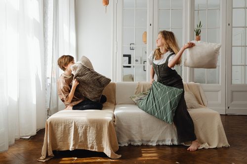 Free Two teenagers joyfully engaged in a playful pillow fight at home, enhancing bonds and fun. Stock Photo