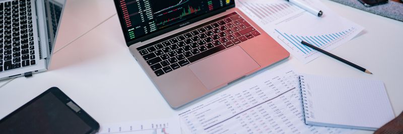 Laptops on a desk displaying stock market charts and financial documents.