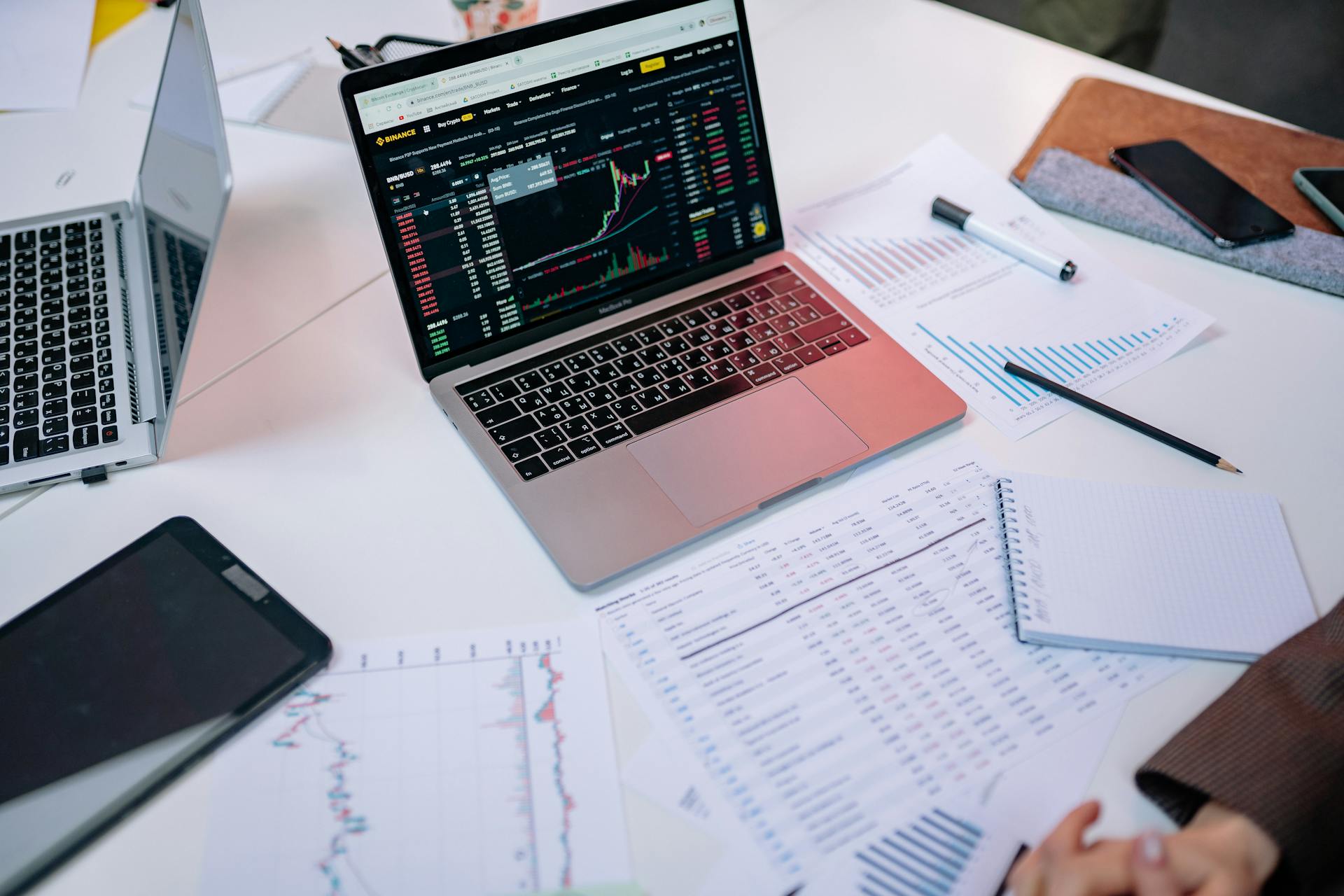 Laptops on a desk displaying stock market charts and financial documents.