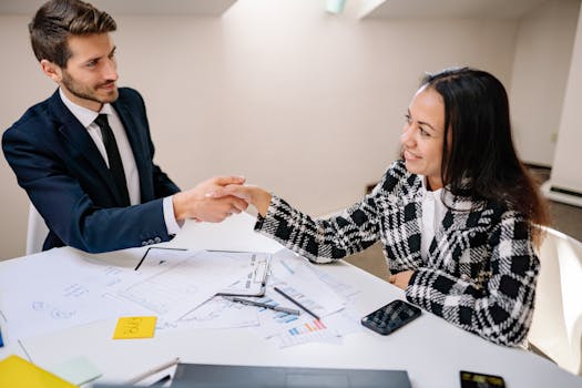 Two business professionals shaking hands over a meeting table, symbolizing cooperation.