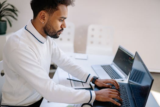 Young professional working diligently on multiple laptops in a modern office setting.