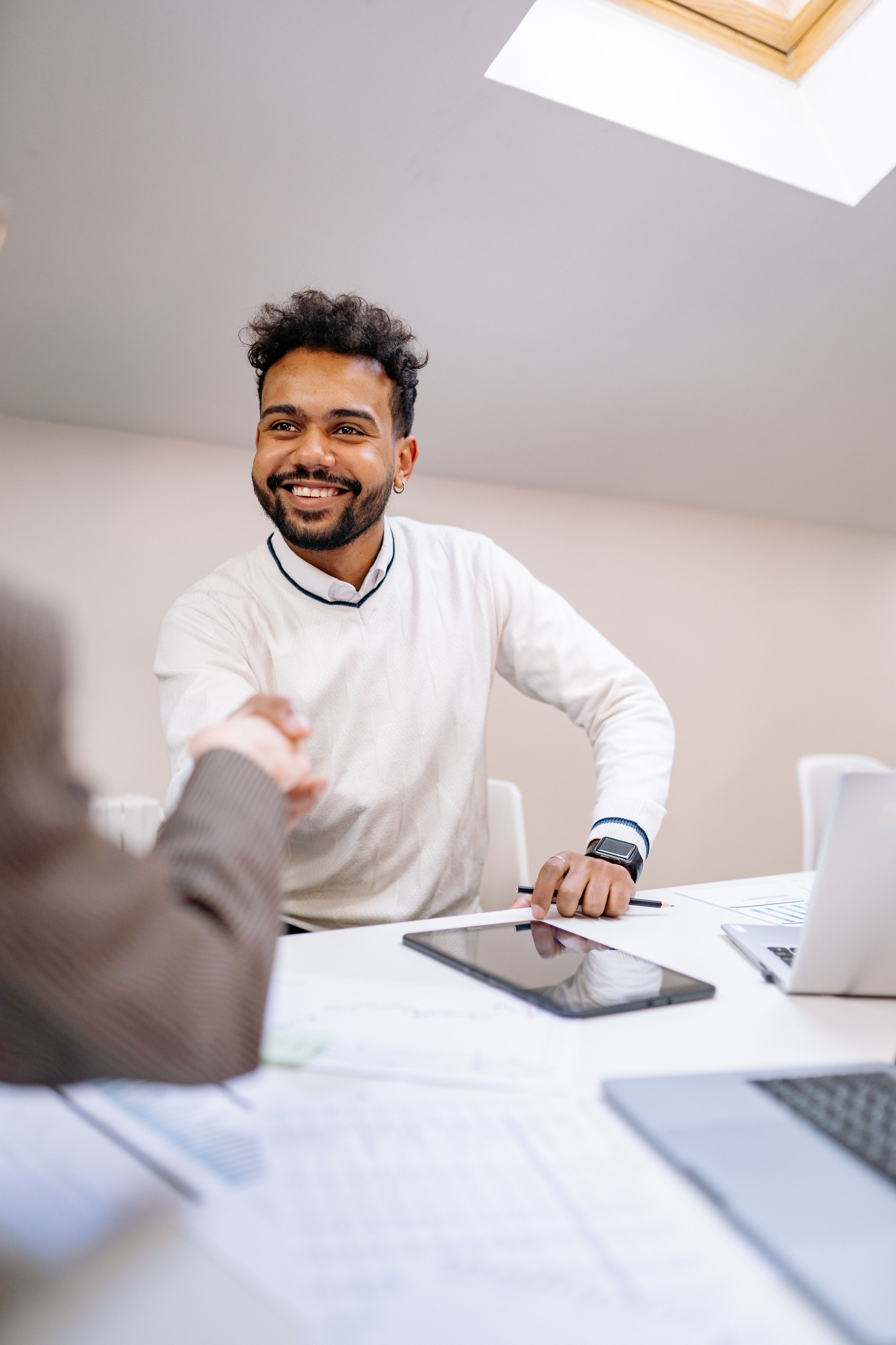 A smiling man in business attire shakes hands across a desk in a modern office.