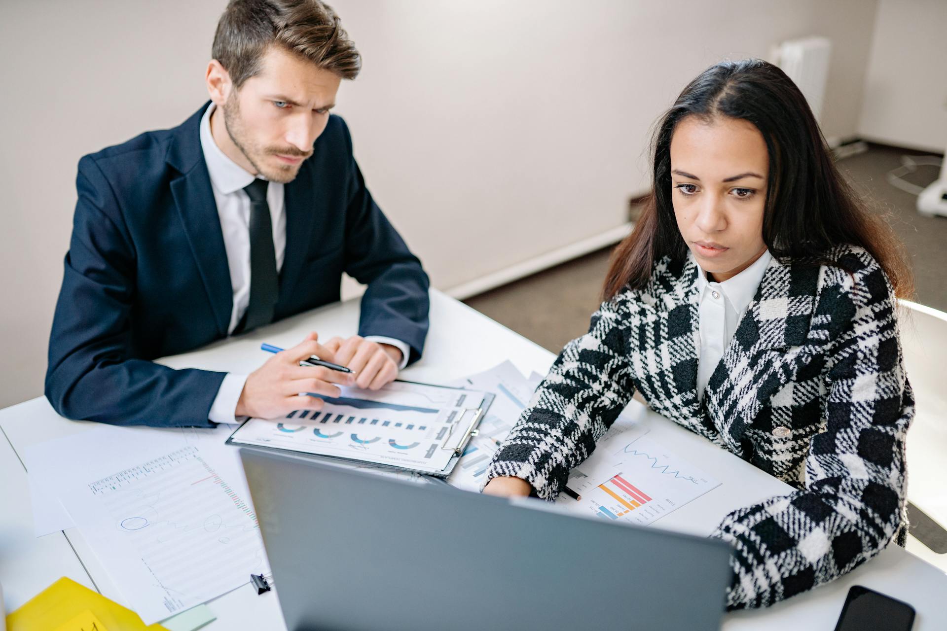 A man and woman collaborate on business analysis at a desk with charts in an office setting.