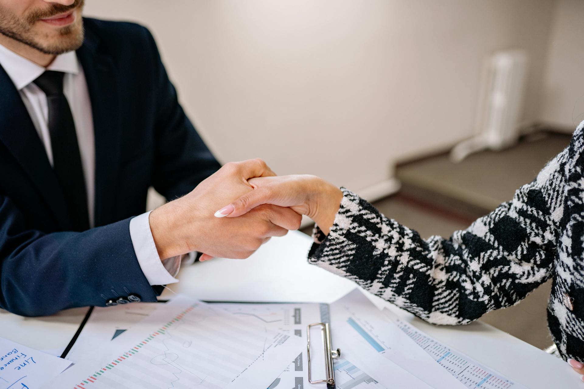 Close-up of a business handshake over documents in an office setting, symbolizing partnership.