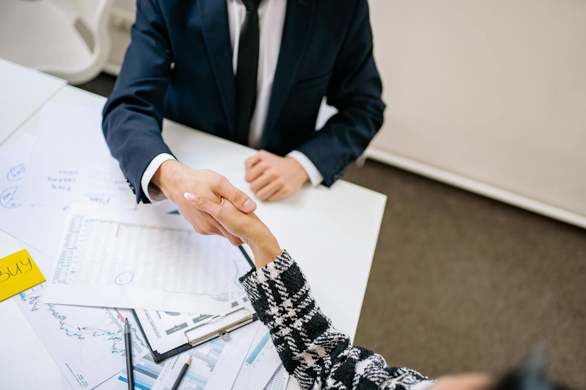 Two professionals formalizing a business agreement with a handshake over a desk.