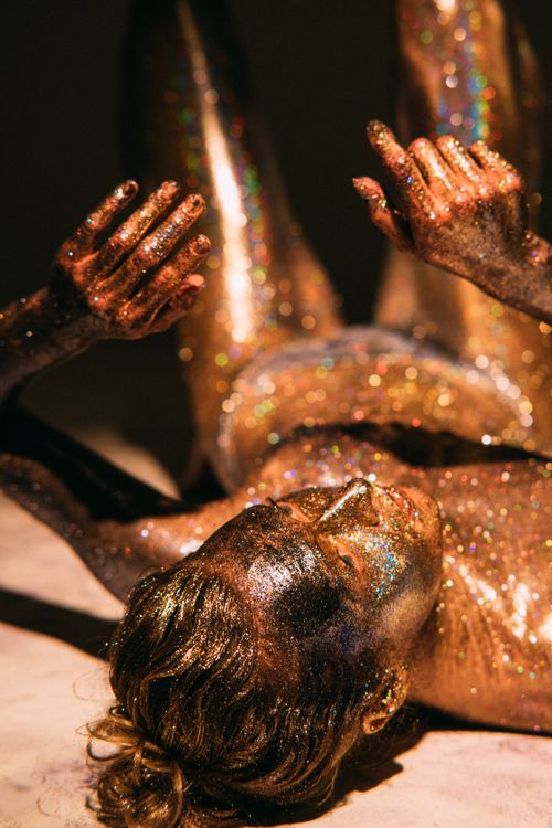 Free A creative studio shoot featuring a model lying down covered in vibrant glitter. Stock Photo