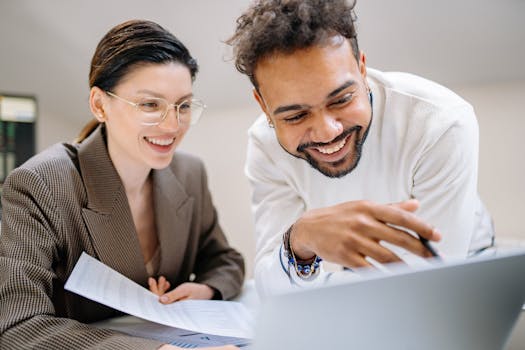 Two smiling colleagues working together on a project, showcasing teamwork and cooperation in a modern office environment.