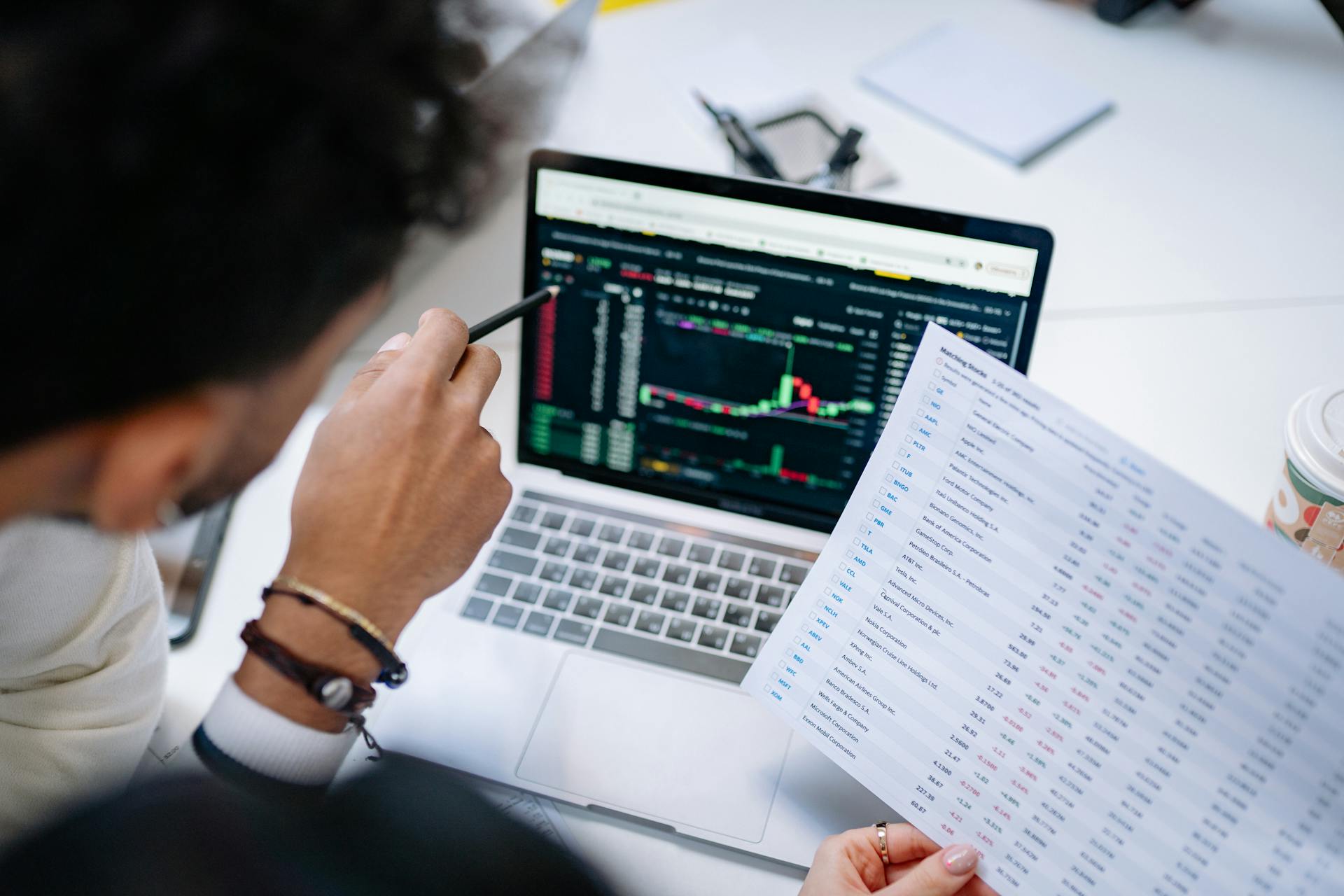 A professional analyzing stock market data on a laptop screen with financial documents.