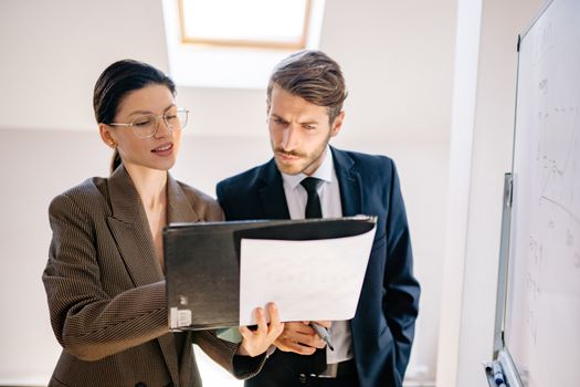 Two professionals collaborate in an office setting, analyzing documents together.