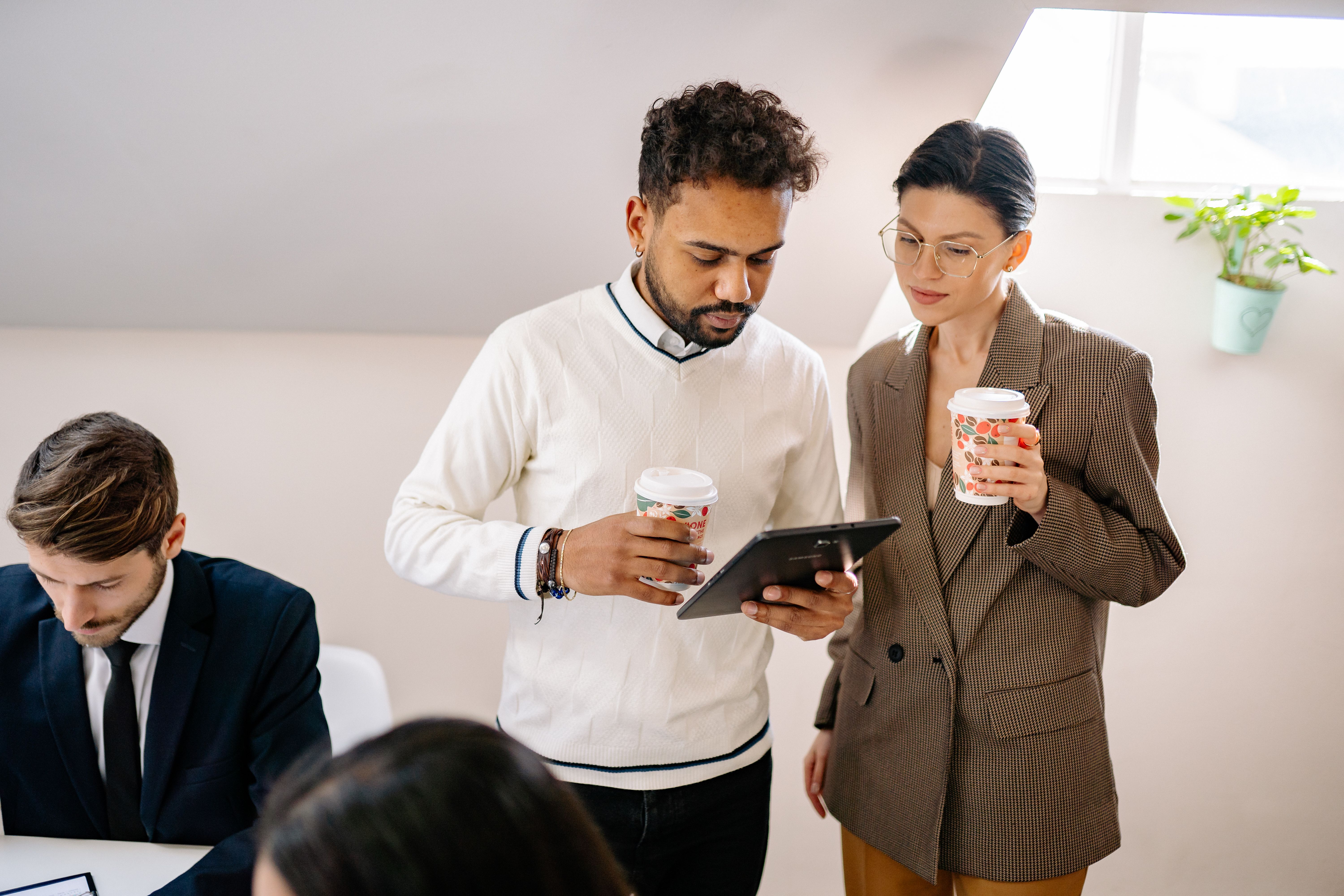 Equipe profissional discutindo sobre café, interagindo com tecnologia digital em ambientes internos.