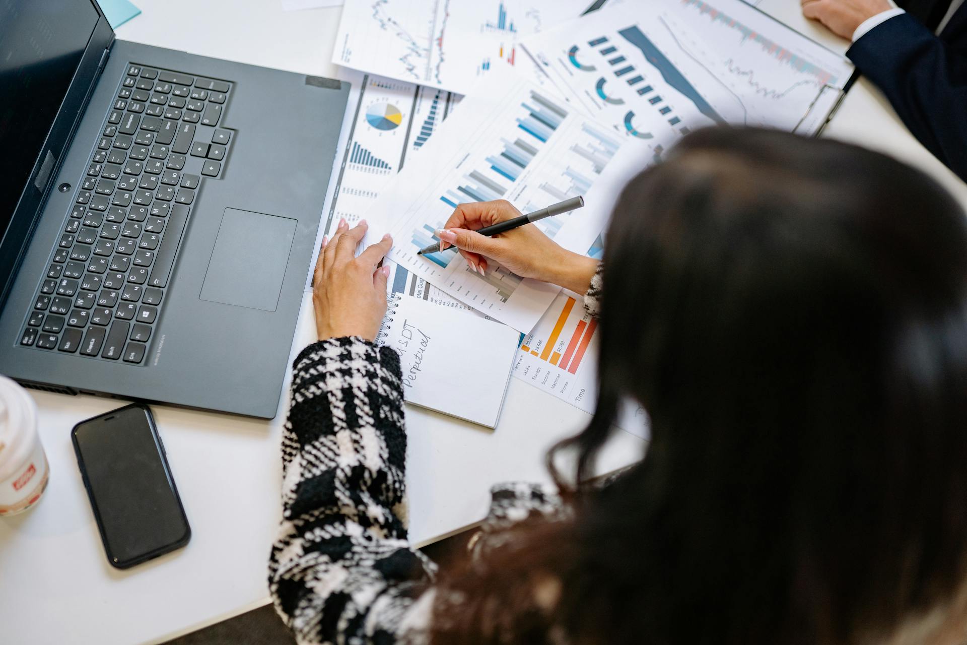 A professional woman reviewing financial charts and graphs with a laptop and smartphone on the desk.