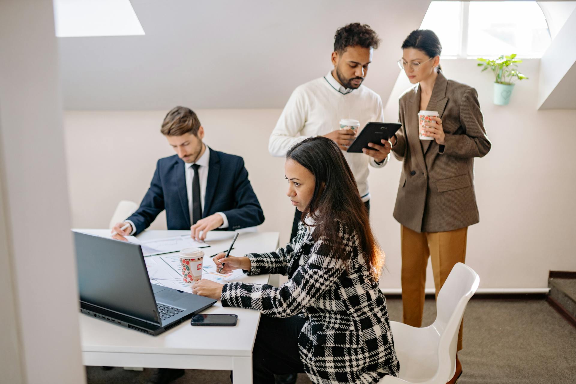 A diverse group of professionals collaborating in a modern office setting, working on laptops and tablets.