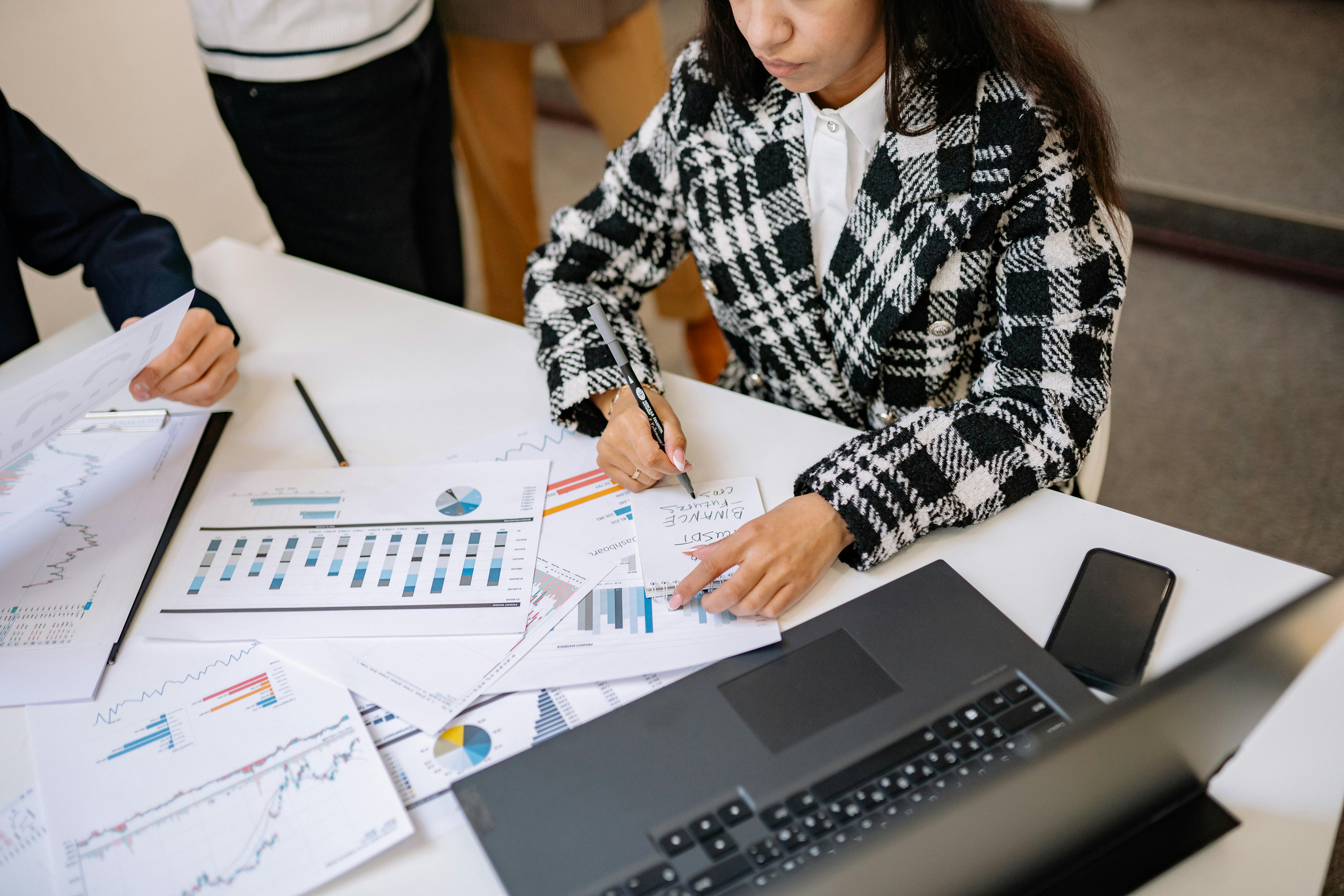 Businesswoman reviewing graphs and charts with colleagues, analyzing financial data in a modern office setting.