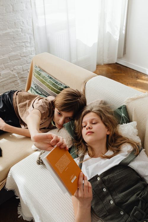 Free Two teenagers reading together on a sofa indoors, creating a warm and relaxed atmosphere. Stock Photo