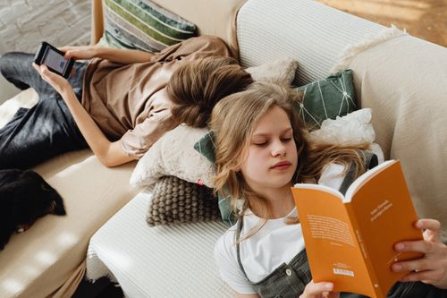 Free Two teenagers relaxing at home, reading and using a tablet on the couch. Stock Photo