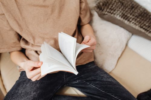 Free Close-up of a person reading a book while sitting on a cozy couch. Stock Photo