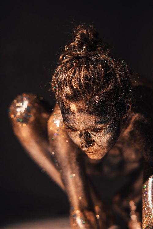 Free A woman covered in glitter poses artistically against a dark background. Stock Photo
