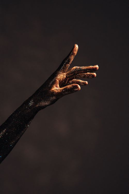 Free A close-up of a hand sprinkled with glitter, artistically lit against a dark backdrop. Stock Photo