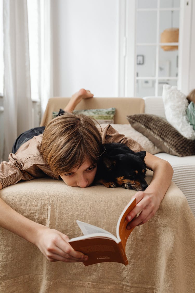 A Black Dog Sleeping Beside A Boy Reading Book