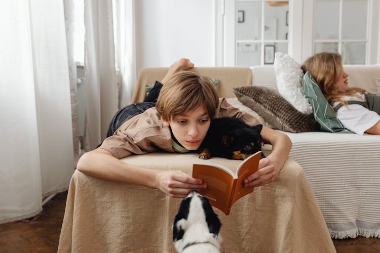 Teenage Boy Lying On Sofa While Reading A Book