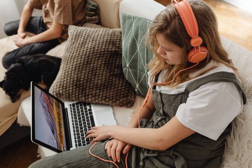 Free Young girl wearing headphones, using laptop on couch, relaxing indoors. Stock Photo