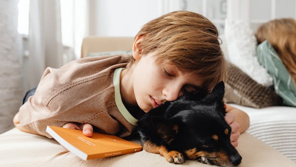 A young boy rests his head on a black dog while holding a book, depicting calmness and companionship.