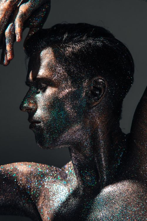 Free Artistic side view portrait of a shirtless man covered in shimmering glitter, creating a dramatic effect. Stock Photo