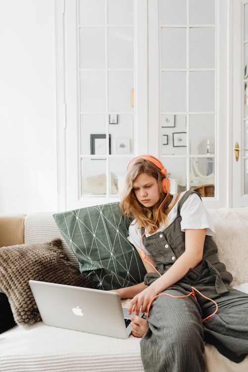 Free Young woman sitting on a sofa using a laptop and headphones indoors. Modern lifestyle concept. Stock Photo