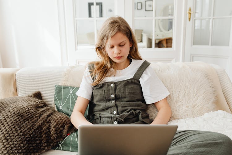 A Teenager Using A Laptop While Sitting On The Sofa