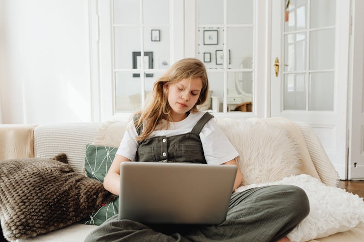 A Teenager Using A Laptop While Sitting On The Sofa