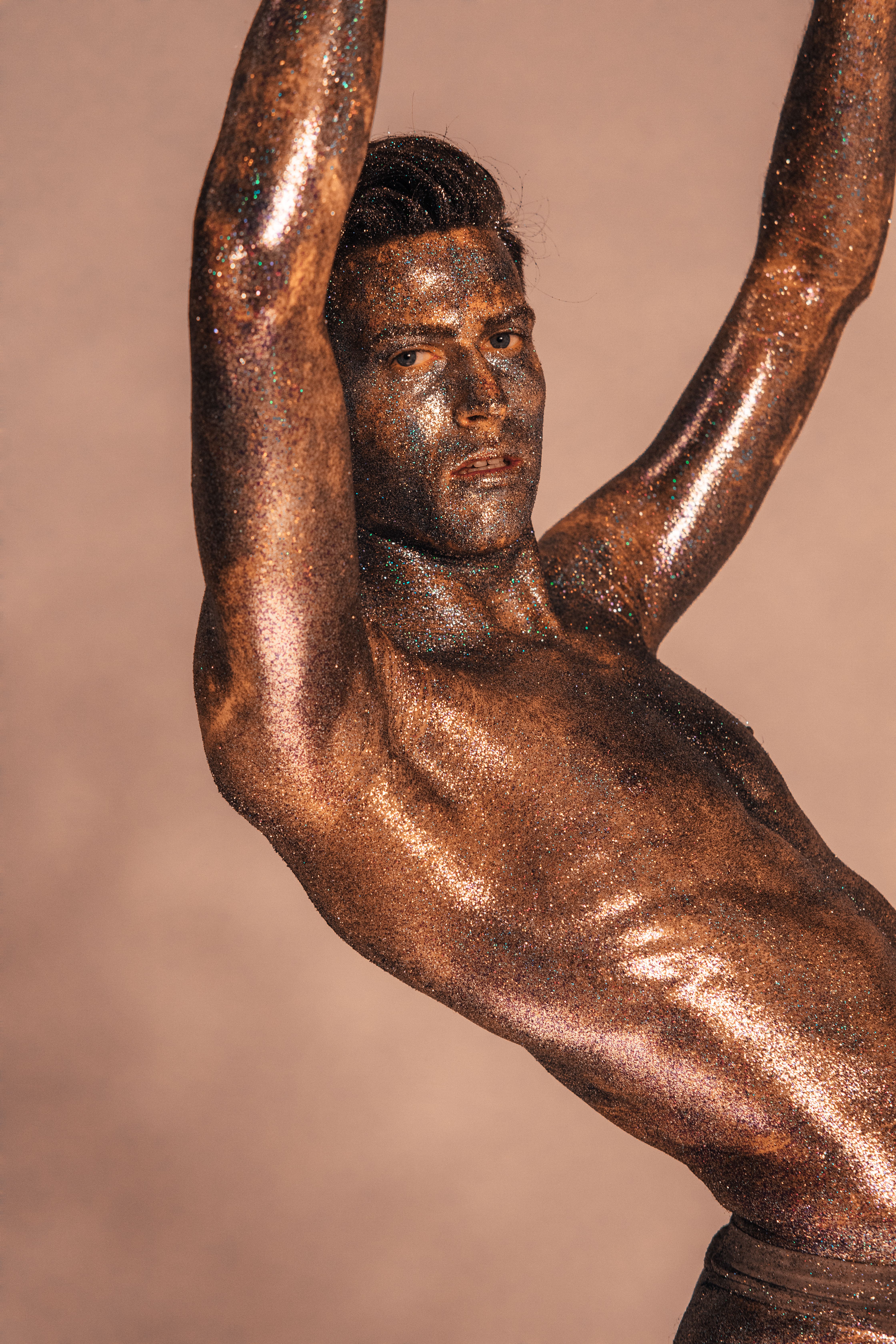 Artistic portrait of a man with shimmering glitter on skin, showcasing a dramatic pose.