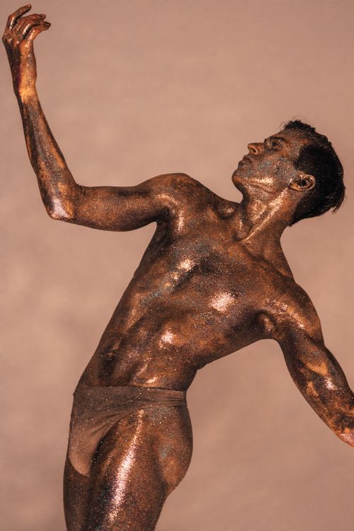 Free Artistic male model posing with bronze body paint, showcasing elegance and grace. Stock Photo