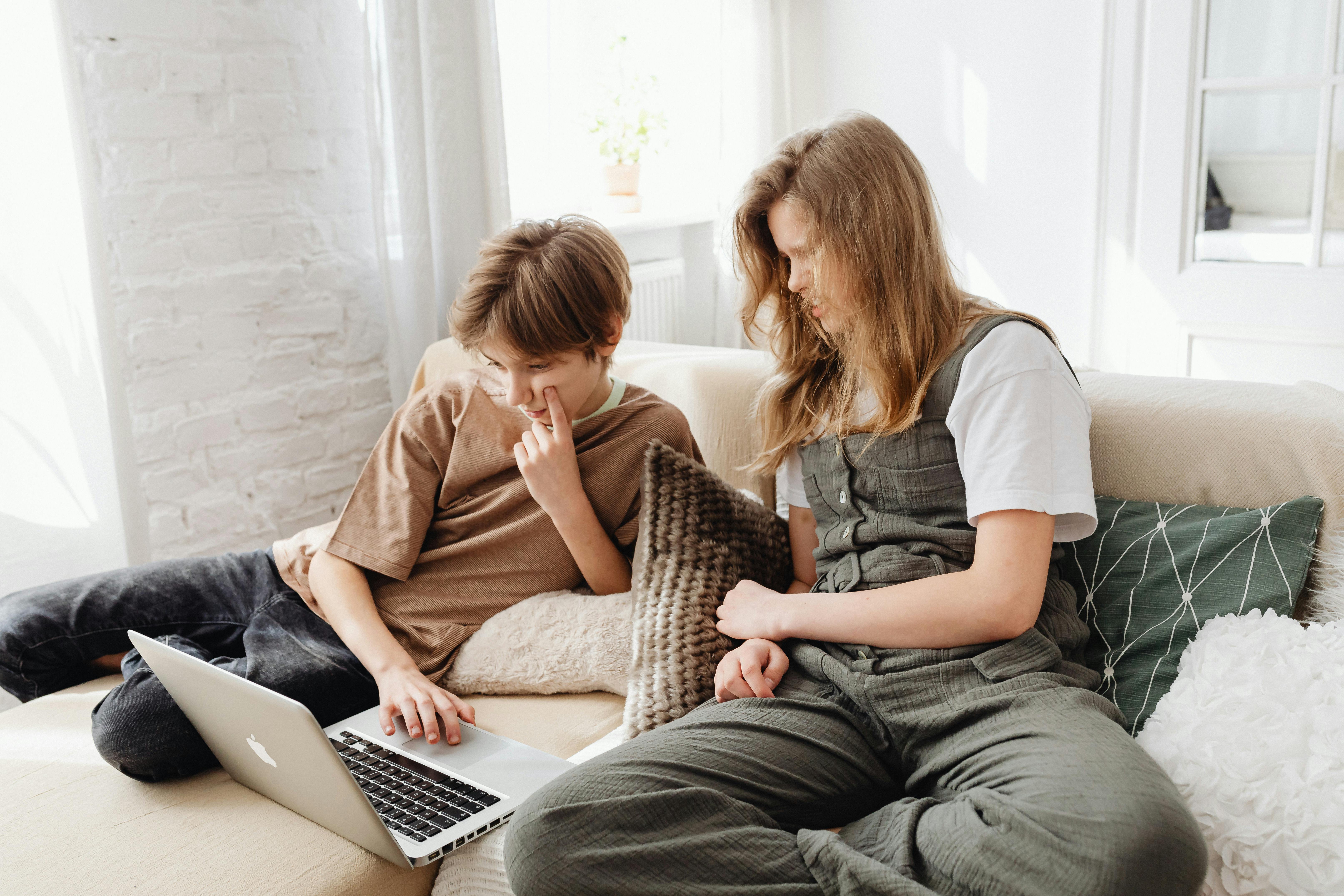Two children enjoying leisure time on a sofa, using a laptop together indoors.