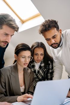 A diverse group of professionals collaborating on a laptop at work.